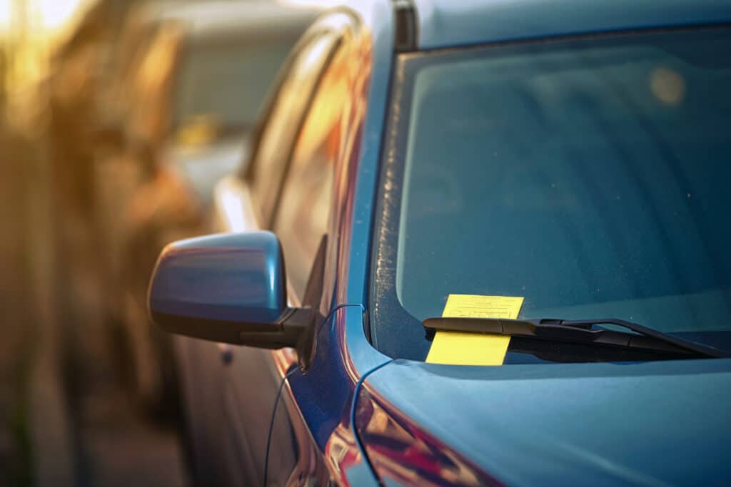 Yellow parking ticket over car windscreen wiper. Payment notice for parking penalty secured under car's windshield wiper. Parking charge notice